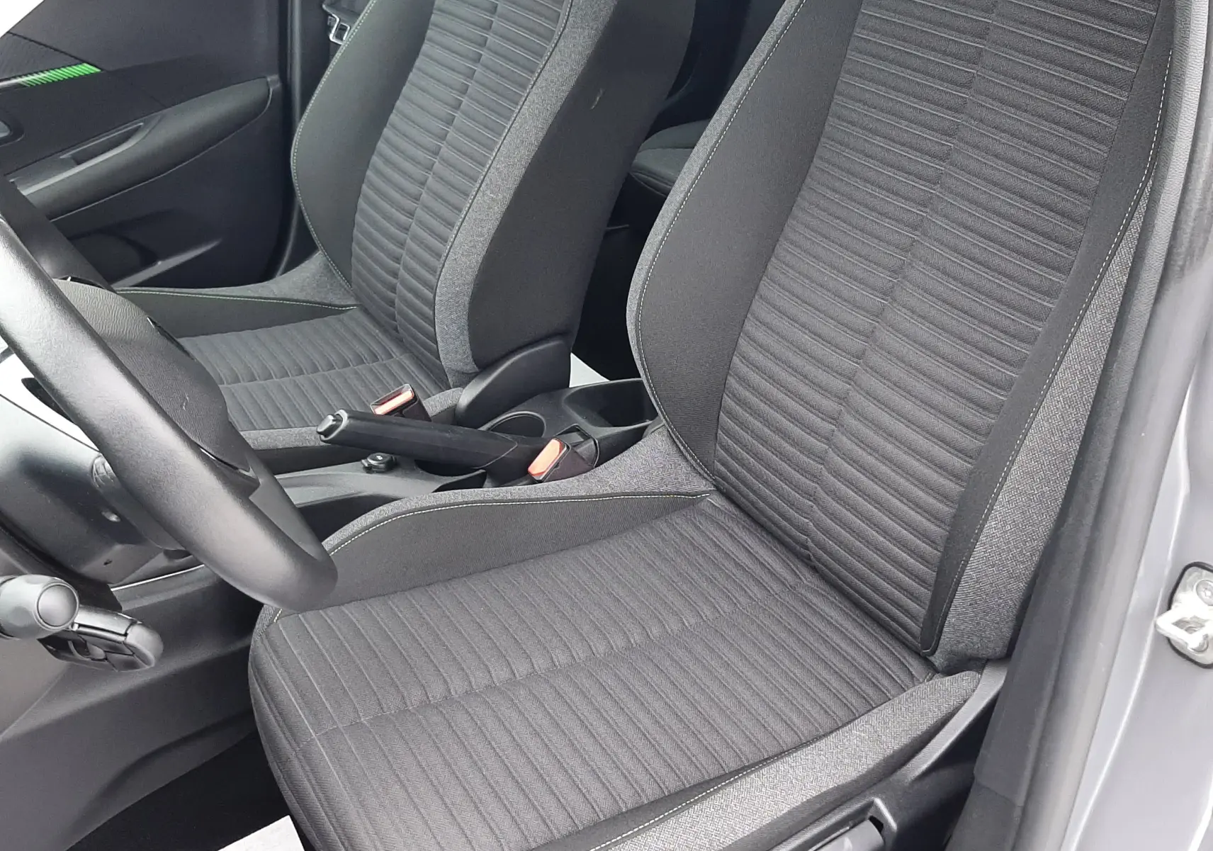 Vue intérieure rapprochée des sièges avant en tissu gris foncé de la Peugeot 208 2024, porte ouverte côté conducteur.