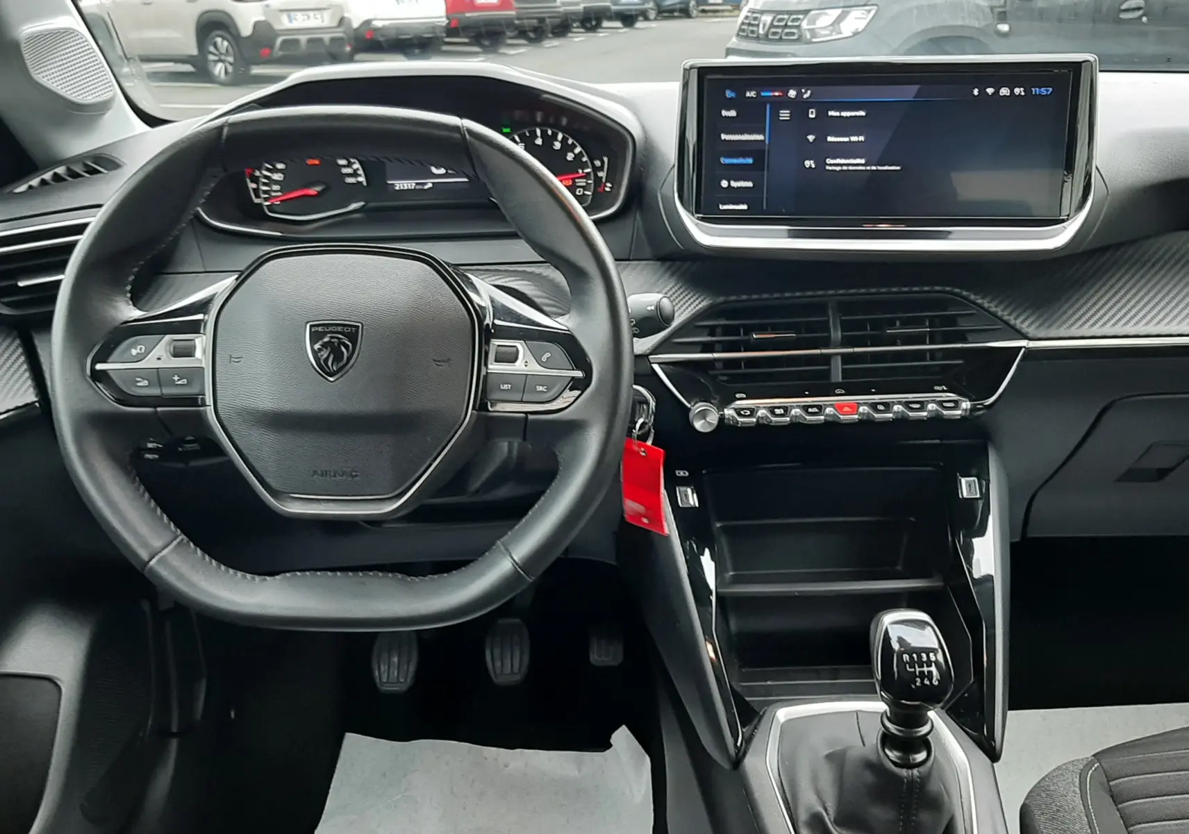 Vue intérieure avant de la Peugeot 208 2024, tableau de bord noir avec volant compact et écran tactile central.