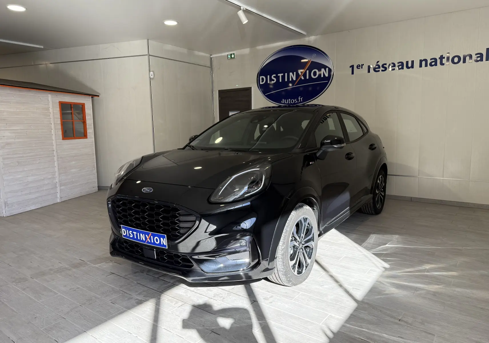 Ford Puma noir agate en 3/4 avant droit, avec calandre large et jantes alliage distinctives, en intérieur showroom.