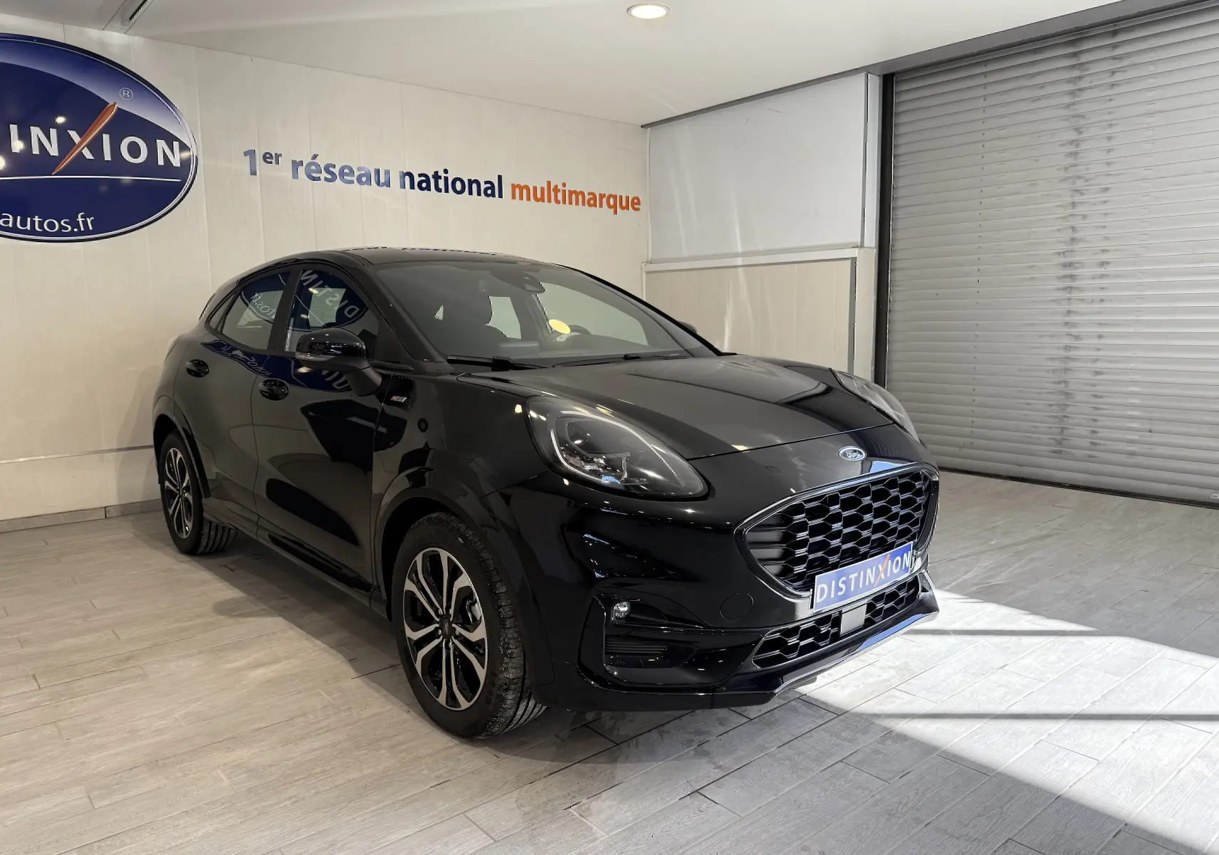 Vue 3/4 avant gauche d'une Ford Puma noire Agate avec calandre large et jantes alliage distinctives en intérieur showroom.