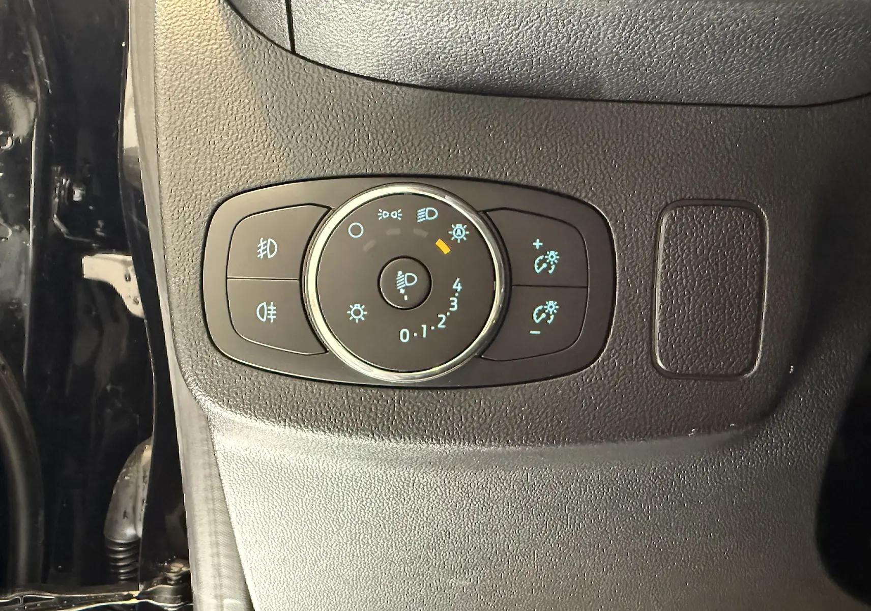 Gros plan sur le bouton de réglage des phares et des feux antibrouillard dans l’habitacle noir du Ford Puma noir agate.