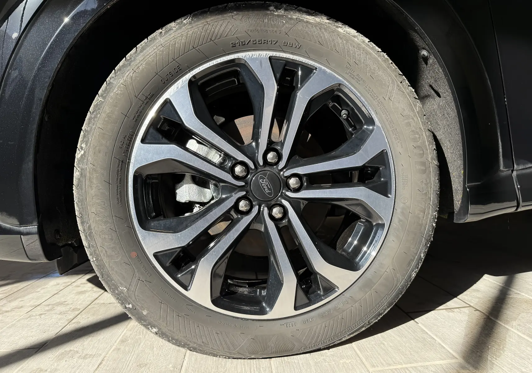 Gros plan sur la roue avant droite du Ford Puma noir Agate, mettant en valeur la jante alliage bicolore et le logo Ford central.