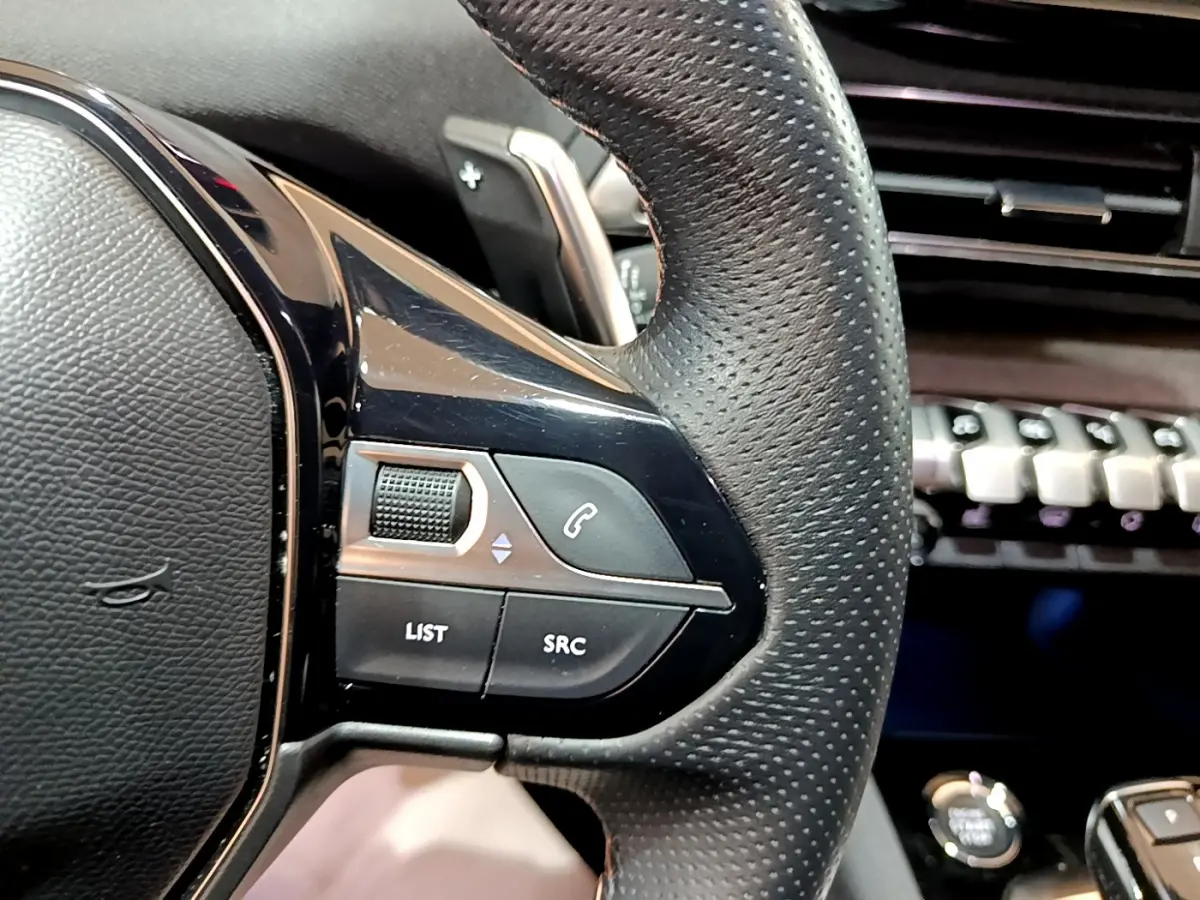 Gros plan sur le côté gauche du volant cuir noir du Peugeot 3008 2023 avec commandes audio et téléphone intégrées.