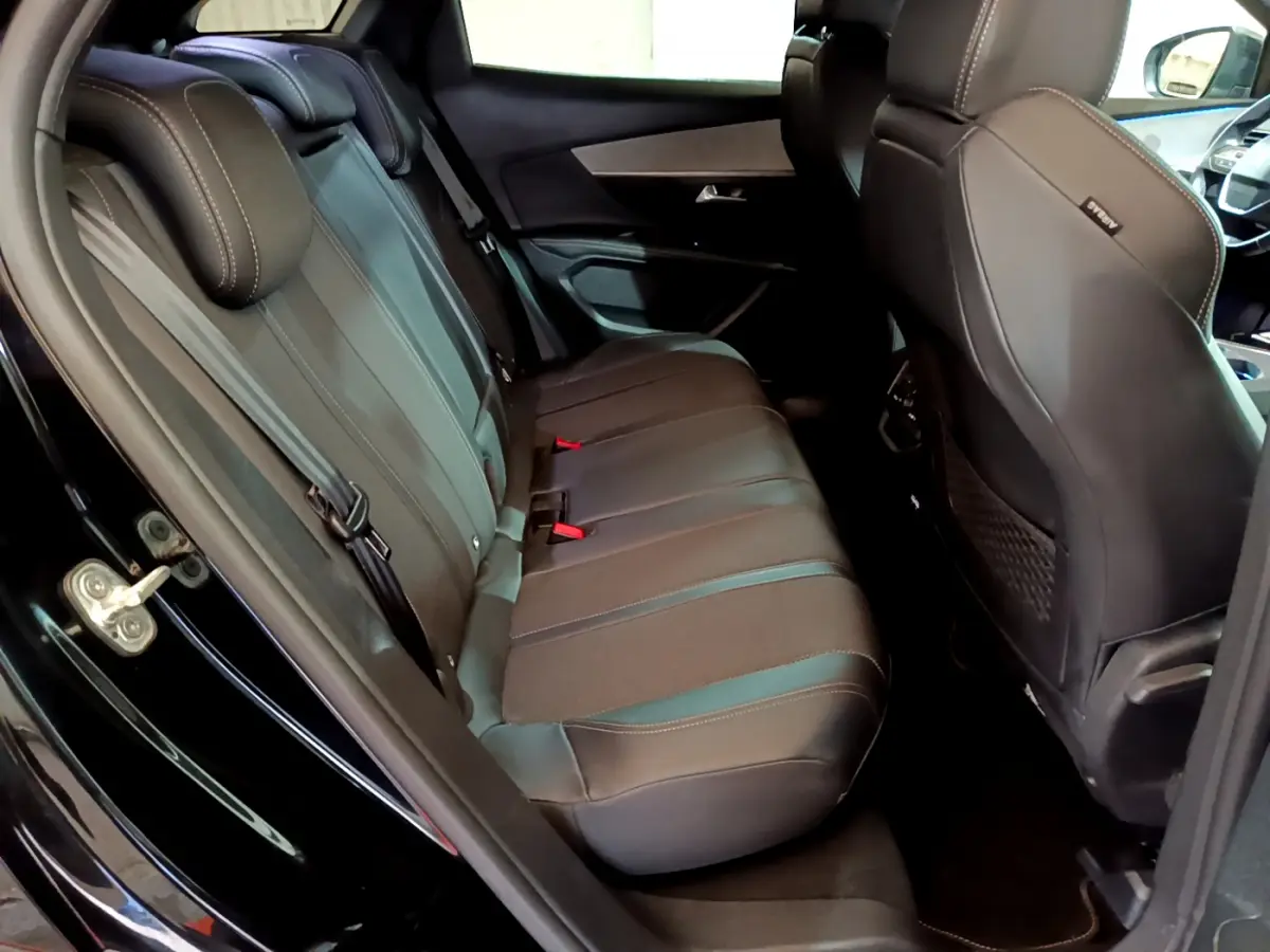 Vue côté gauche sur l'intérieur arrière noir du Peugeot 3008 2023 avec sièges en cuir et ceintures visibles