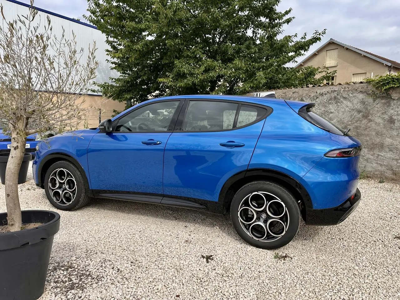 Vue de profil côté gauche d'un Alfa Romeo Tonale 1.5 mHEV Sprint bleu métallisé garé sur gravier, avec jantes distinctives.