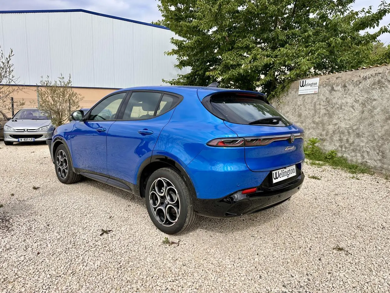 Vue 3/4 arrière droite d'une Alfa Romeo Tonale bleu métallisé avec jantes distinctives et feux arrière fins.
