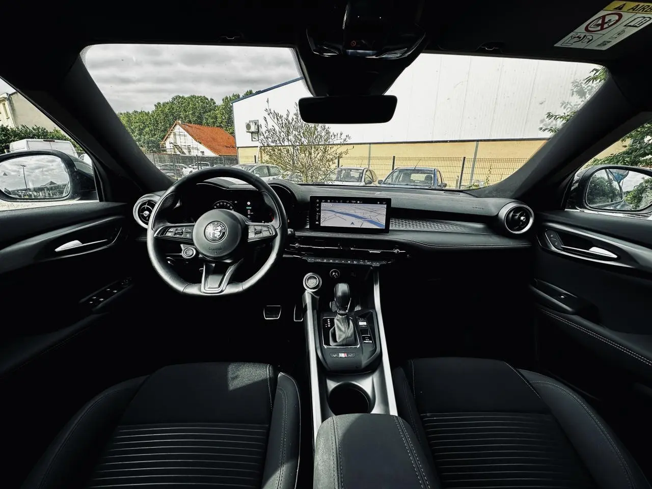 Vue intérieure avant de l'Alfa Romeo Tonale 2024, tableau de bord noir avec écran tactile et volant sport cuir.