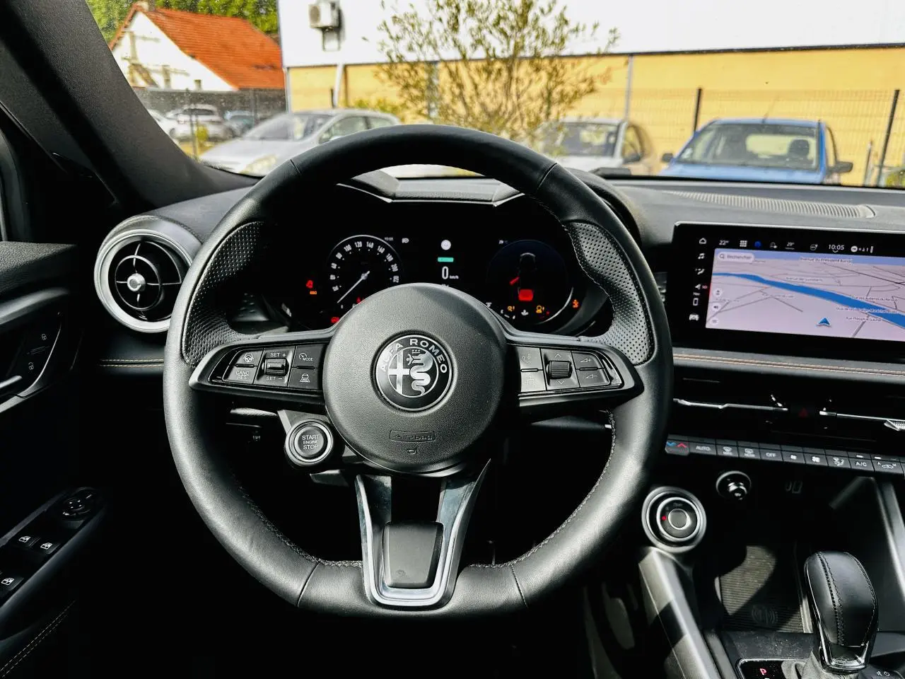 Vue intérieure centrée sur le volant cuir noir de l'Alfa Romeo Tonale 2024 avec tableau de bord digital et écran tactile GPS.