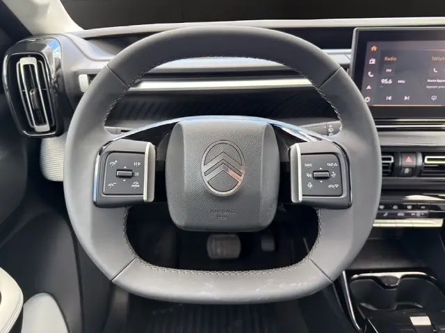 Vue rapprochée du volant multifonction noir de la Citroën C3 Aircross Electric 2025 avec tableau de bord numérique en arrière-plan.