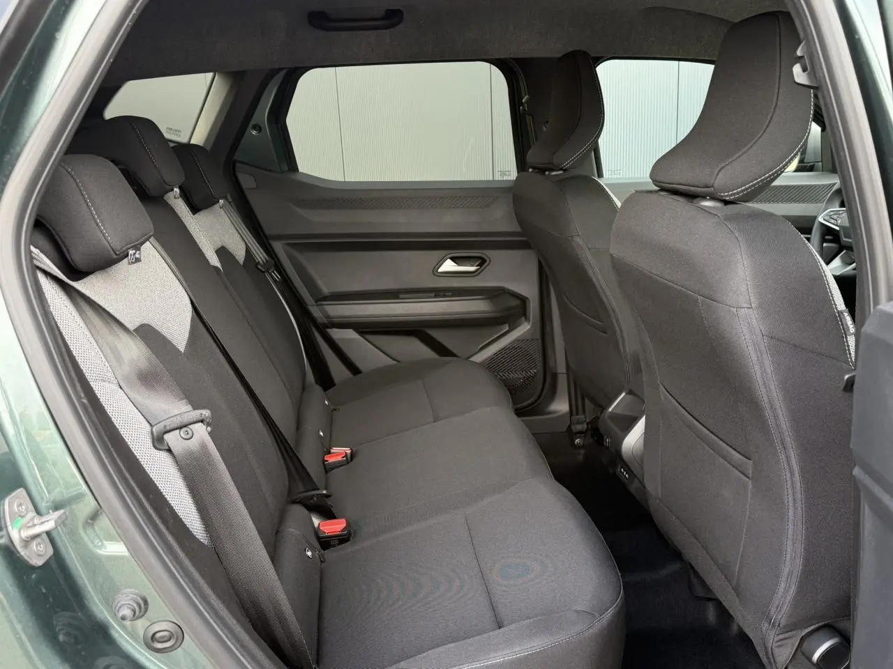 Vue latérale intérieure sur la banquette arrière noire du Dacia Duster Vert Cèdre avec ceinture de sécurité visible.