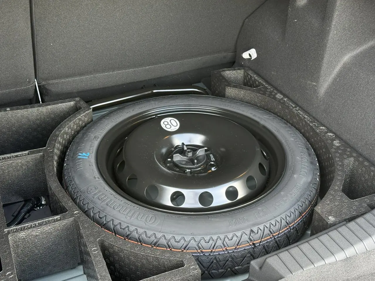 Gros plan sur la roue galette noire dans le coffre du Dacia Duster Vert Cèdre, version hybride 2026.