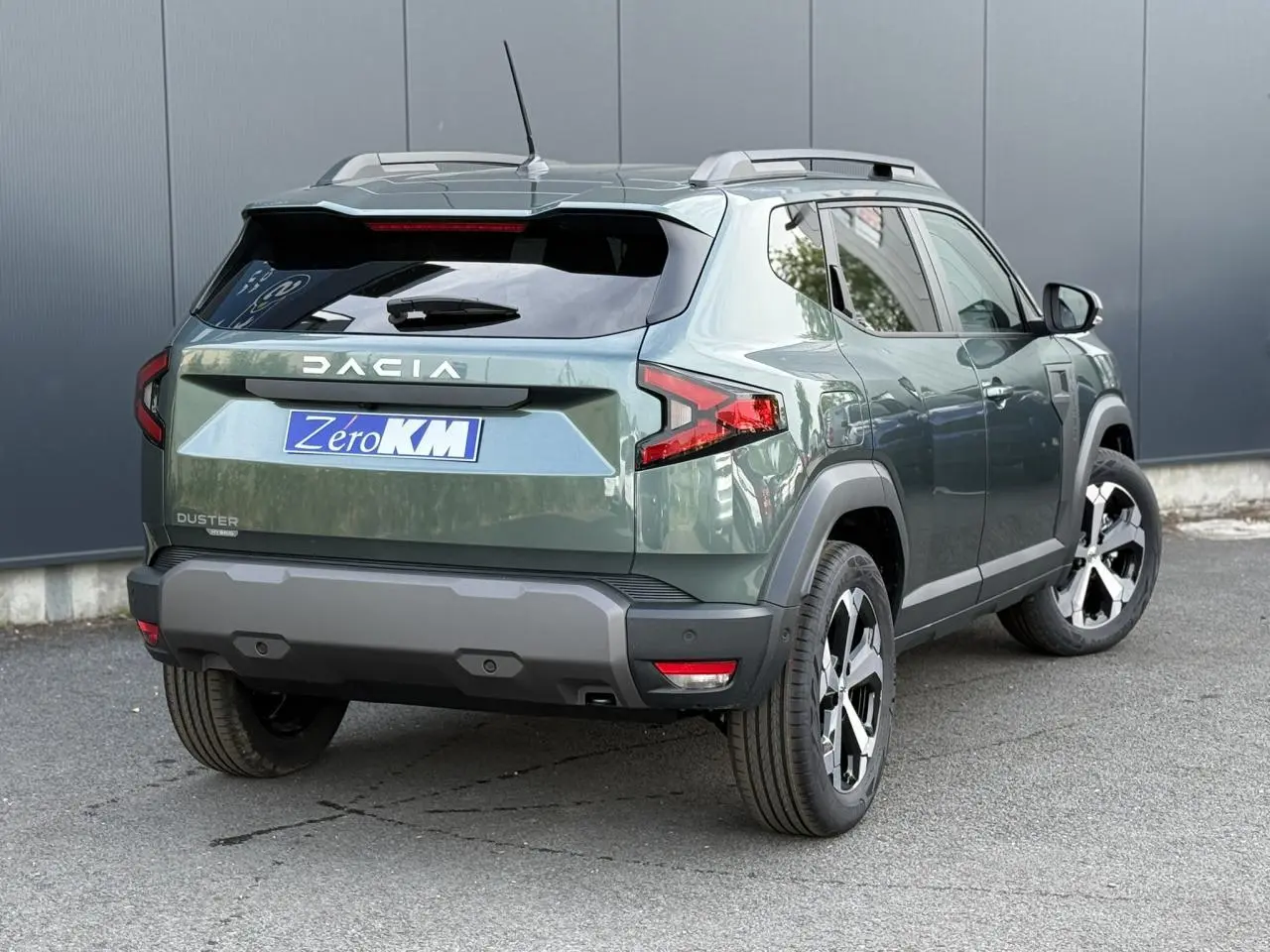 Vue 3/4 arrière droite du Dacia Duster 2026 vert cèdre avec jantes alliage diamantées et barres de toit argentées.