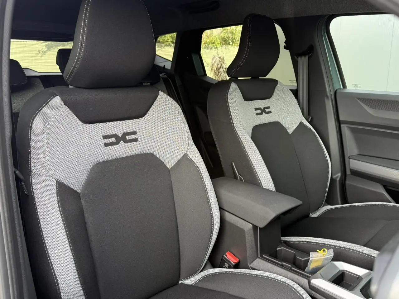 Vue intérieure des sièges avant gris et noirs du Dacia Duster 2026, avec accoudoir central et finitions contrastées.