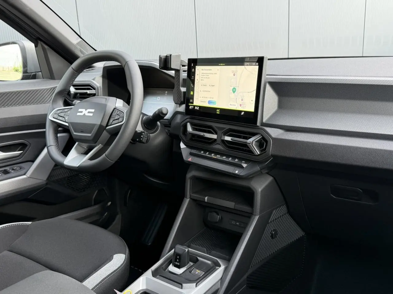 Vue intérieure côté conducteur du Dacia Duster 2026, avec tableau de bord noir et écran tactile central affichant la navigation.