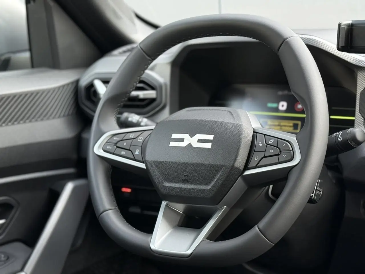 Vue rapprochée du volant noir du Dacia Duster 2026 avec commandes intégrées et tableau de bord digital en arrière-plan.