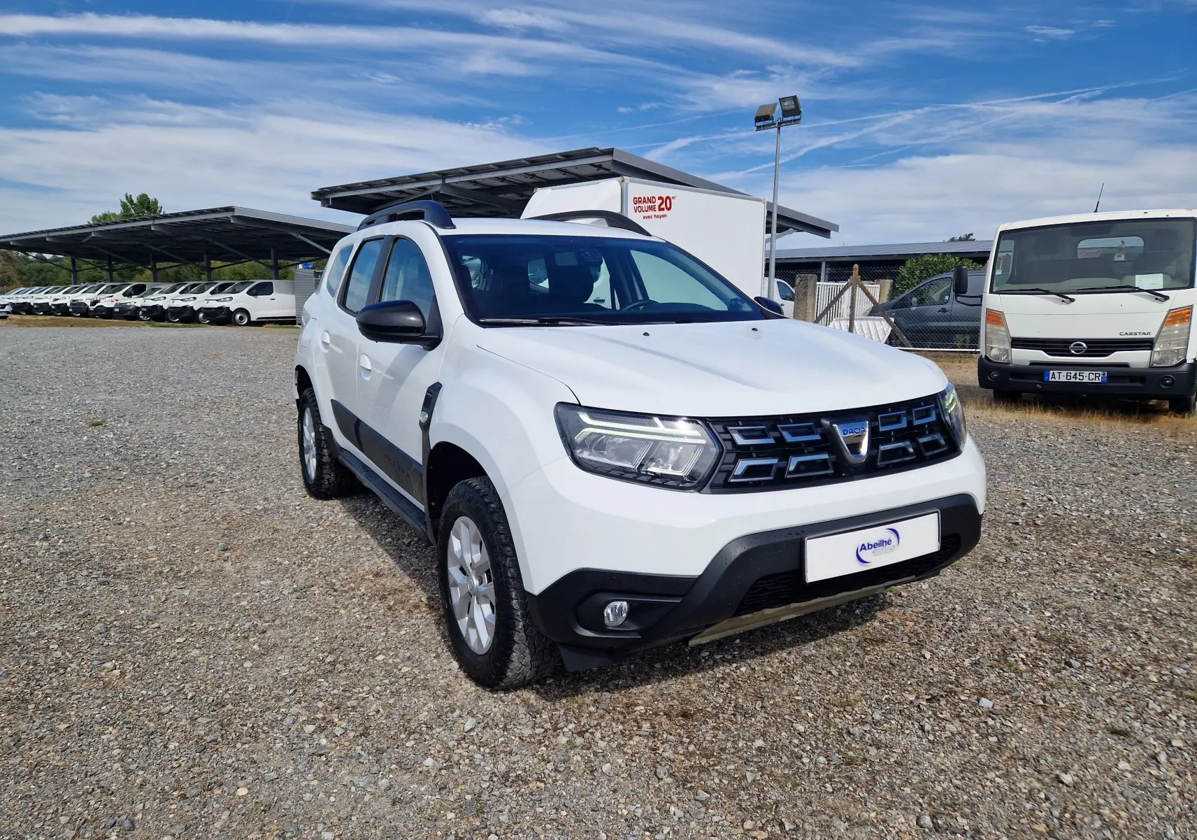 Dacia Duster 4x4 blanc vue 3/4 avant droit sur parking gravillonné avec calandre noire et jantes argentées.
