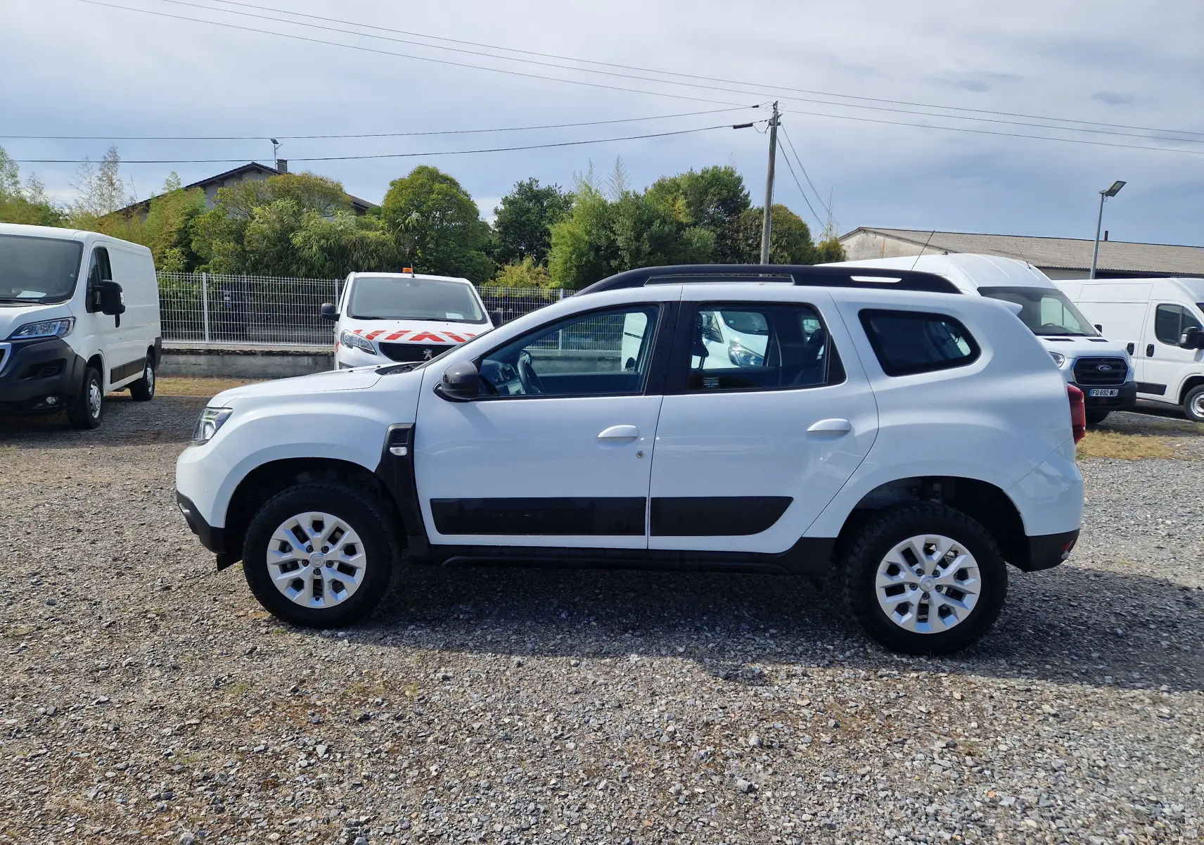 Profil droit du Dacia Duster 4x4 blanc 2022 avec protections noires et jantes alliage 16 pouces visible en extérieur.