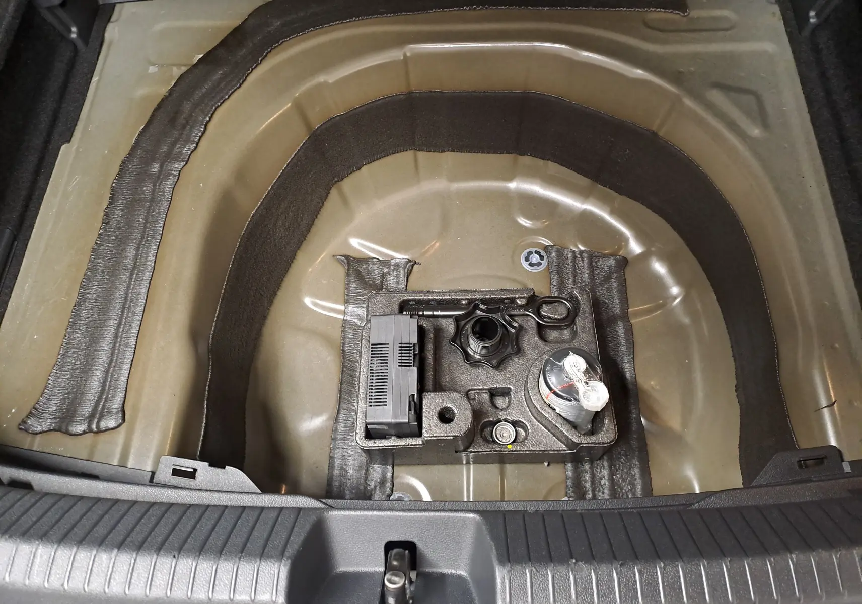 Vue plongeante sur le coffre ouvert d’un Volkswagen Taigo noir intense, montrant le rangement sous plancher avec kit de réparation pneus.