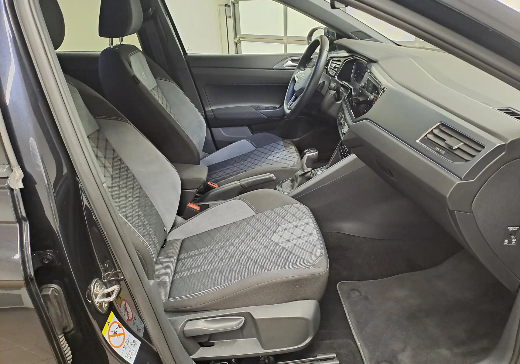 Vue intérieure côté conducteur du Volkswagen Taigo noir intense 2025, sièges tissu avec motifs géométriques et tableau de bord moderne.