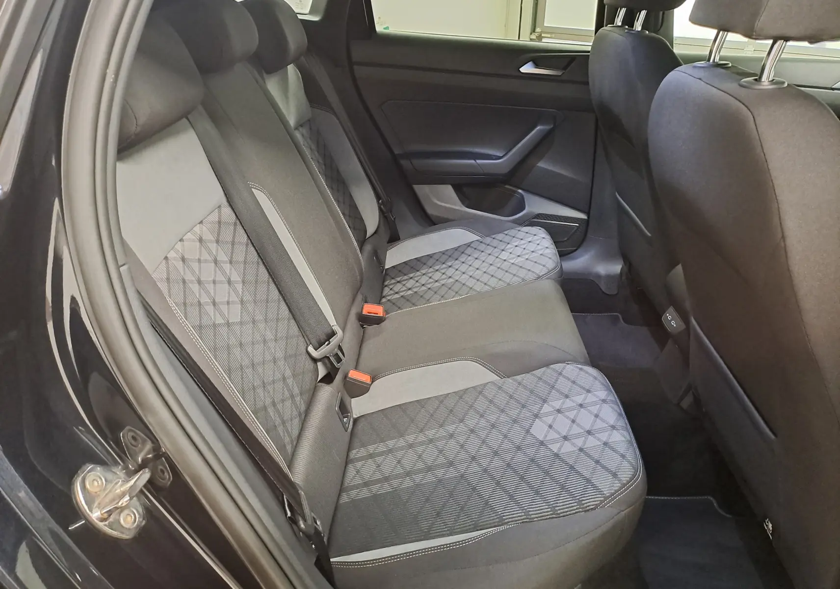 Vue intérieure côté gauche des sièges arrière du Volkswagen Taigo noir intense avec tissu à motifs géométriques et ceintures de sécurité visibles.