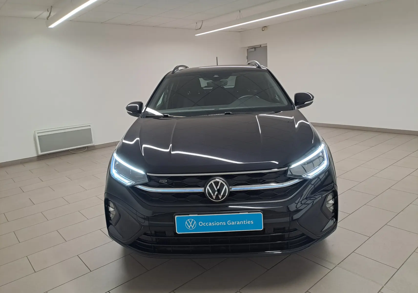 Volkswagen Taigo noir intense 2025 vu de face, avec phares LED allumés et calandre R-Line distinctive.