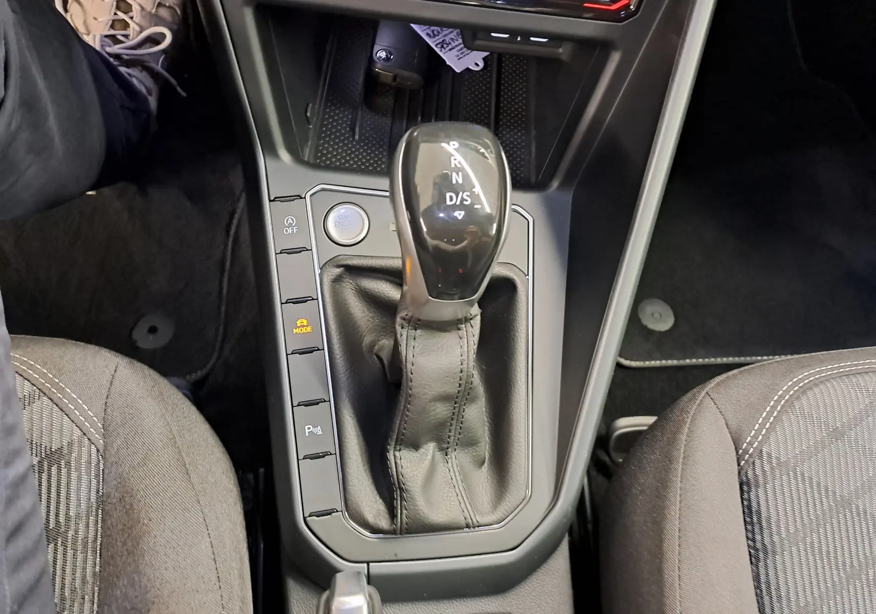 Vue plongeante sur la console centrale du Volkswagen Taigo 2025, avec levier de boîte auto noir et sièges tissu gris.