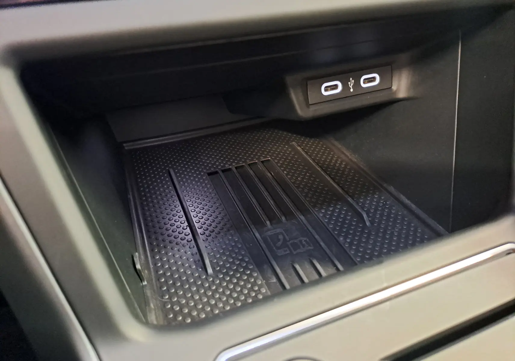 Gros plan sur la zone de rangement avant du Volkswagen Taigo 2025, avec deux ports USB-C visibles au-dessus du tapis antidérapant noir.