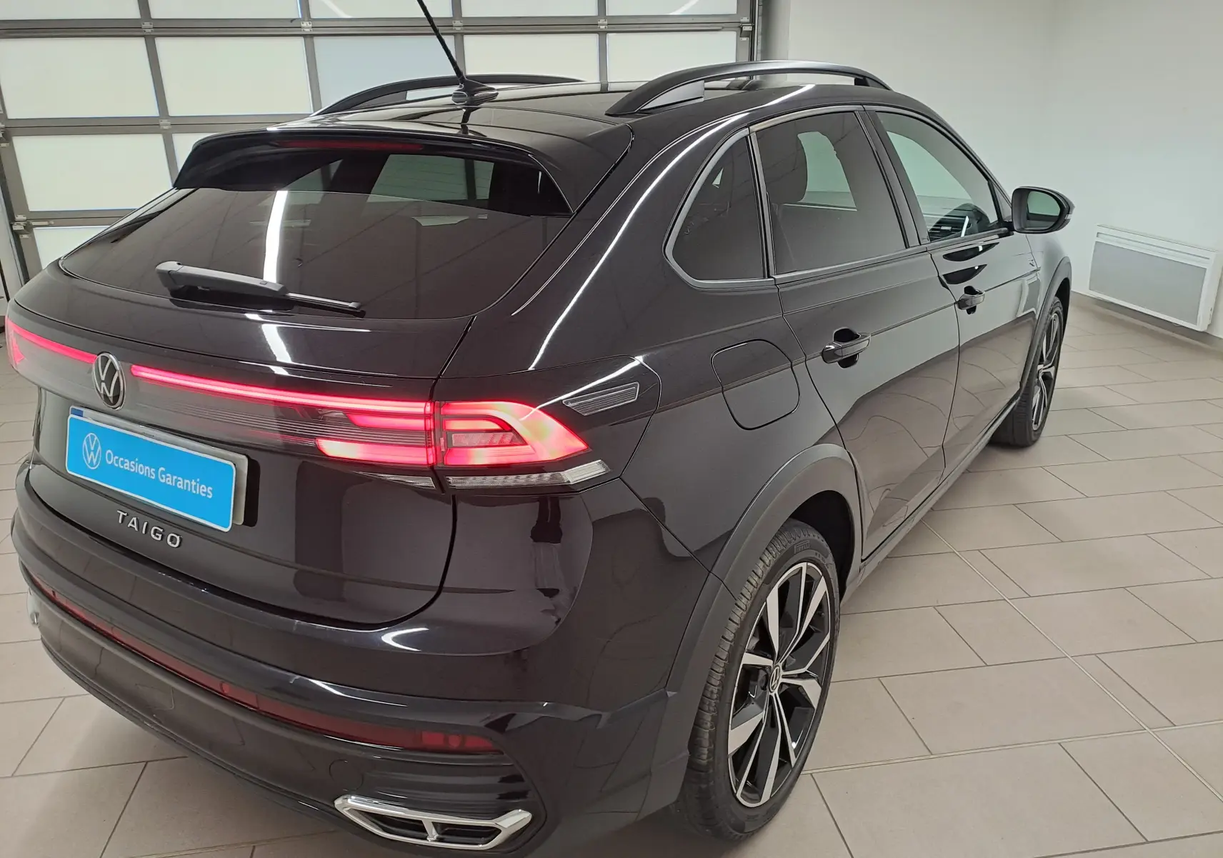 Volkswagen Taigo noir intense vue 3/4 arrière droit, feux arrière allumés et jantes alliage 18 pouces Misano.