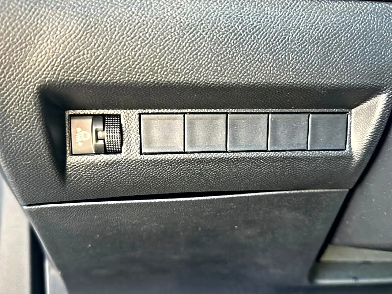 Détail du tableau de bord noir du Peugeot 2008 2025, montrant la molette de réglage des phares et cinq boutons inactifs.