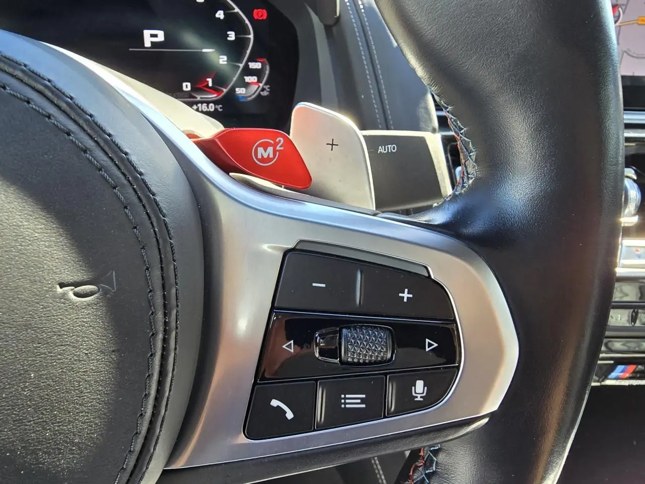 Gros plan sur le volant cuir noir avec palettes M rouges et commandes multifonctions d'une BMW Série 8 Cabriolet M8 Competition.