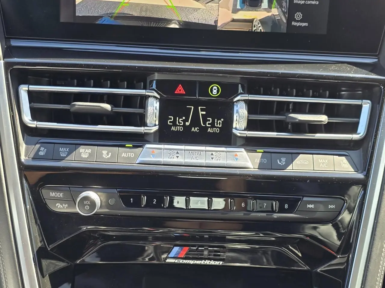Détail de la console centrale noire brillante avec commandes climatisation et logo M8 Competition d'une BMW Série 8 Cabriolet noire.