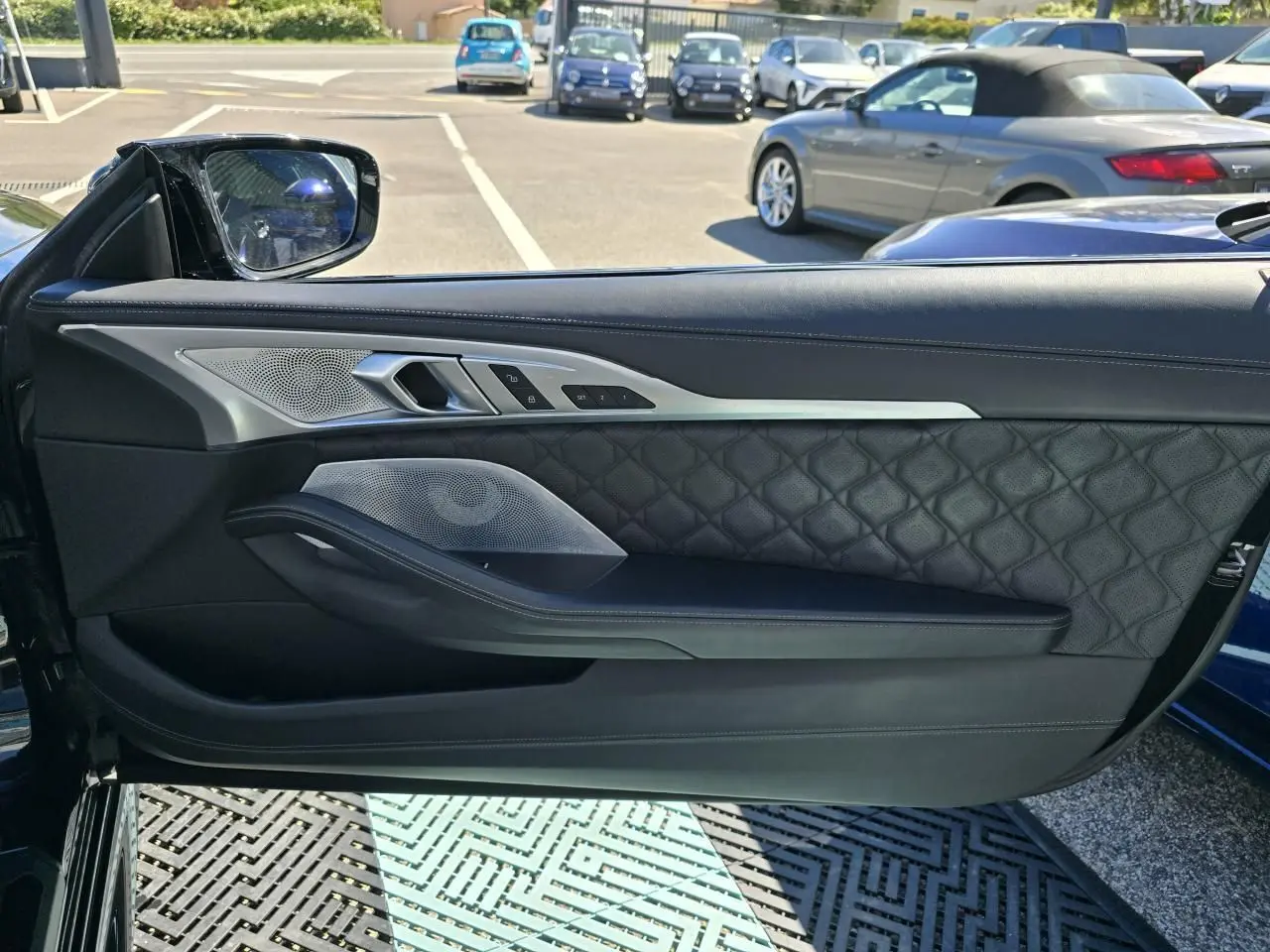 Porte côté gauche ouverte d'une BMW Série 8 Cabriolet noire, avec garniture en cuir matelassé et inserts métalliques.
