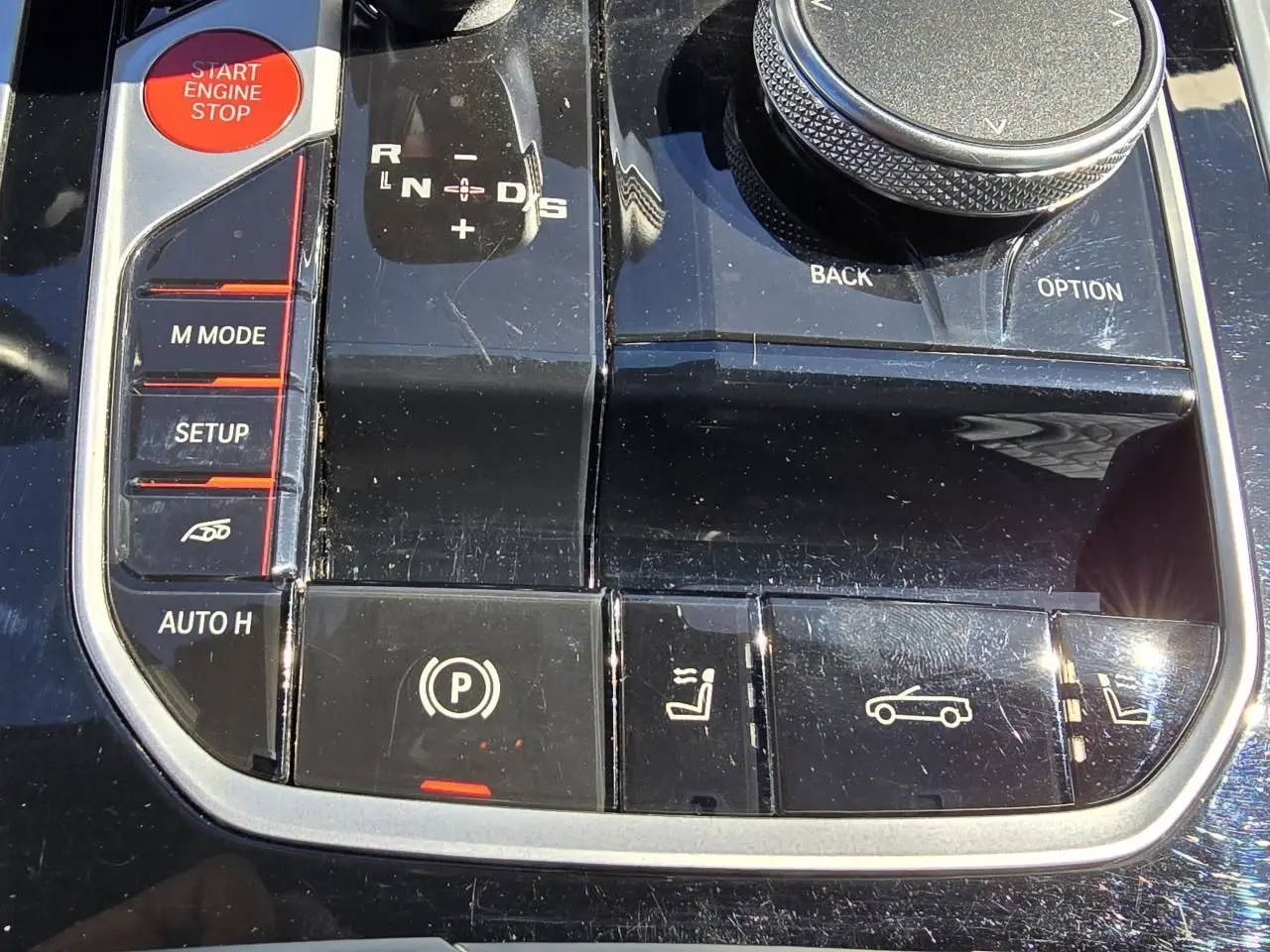 Gros plan sur la console centrale noire laquée du BMW Série 8 Cabriolet M8 Competition avec boutons de commande et molette.