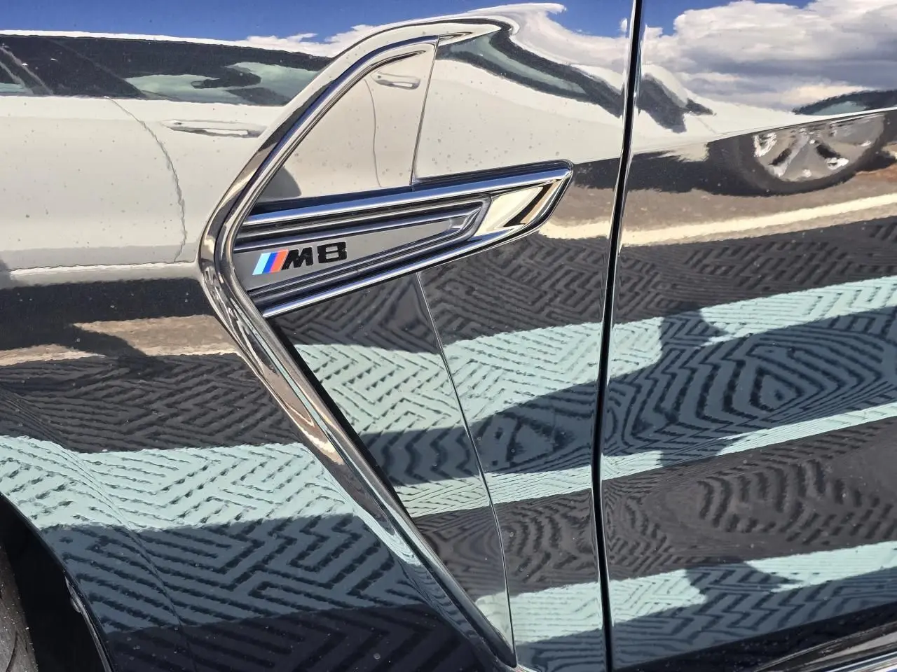 Détail de l'aile avant gauche noire saphir métal d'une BMW M8 avec logo M8 chromé et bleu rouge blanc.