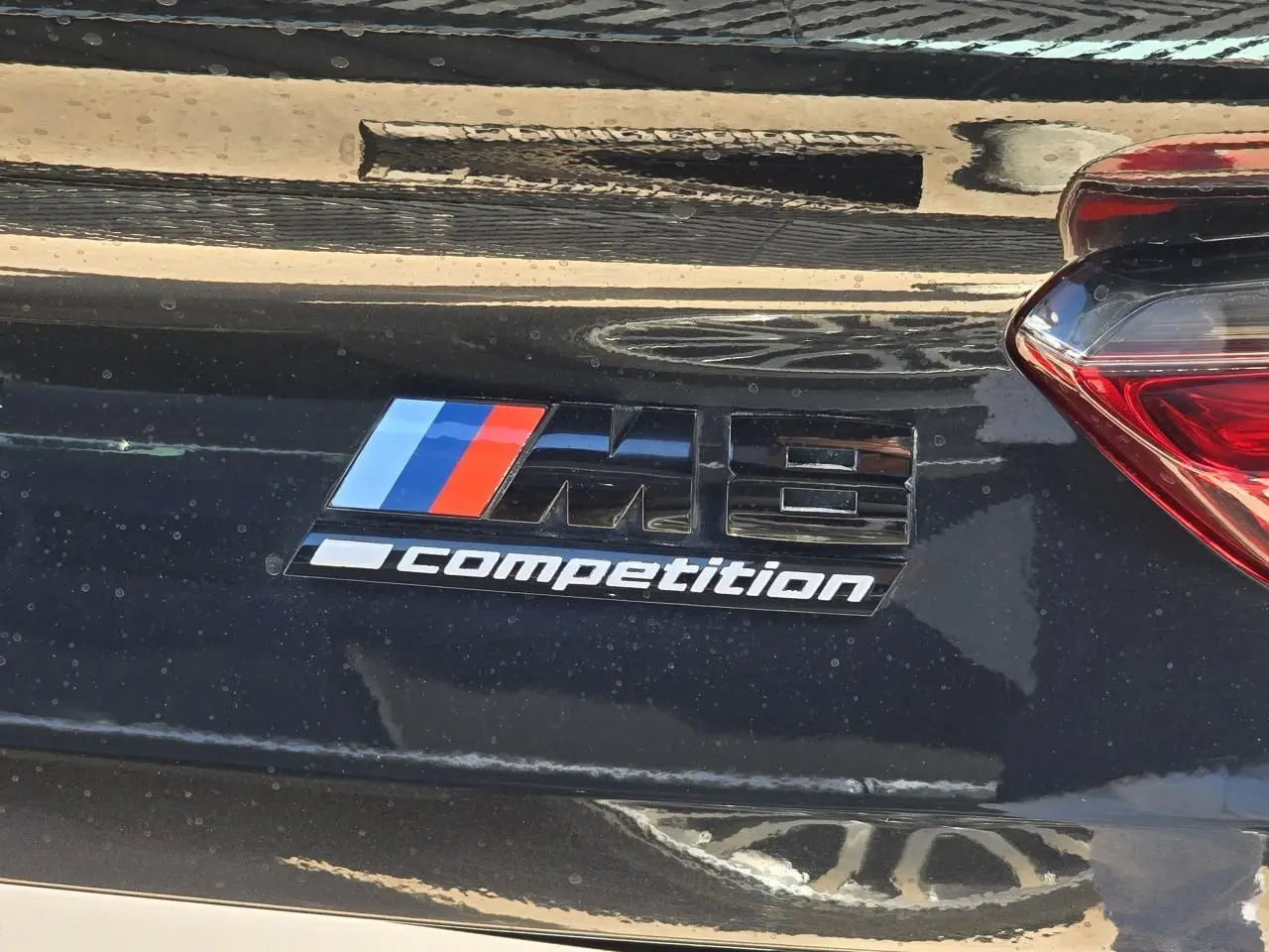 Gros plan sur l'emblème M8 Competition noir brillant sur la malle arrière d'une BMW Série 8 Cabriolet noir saphir métal.