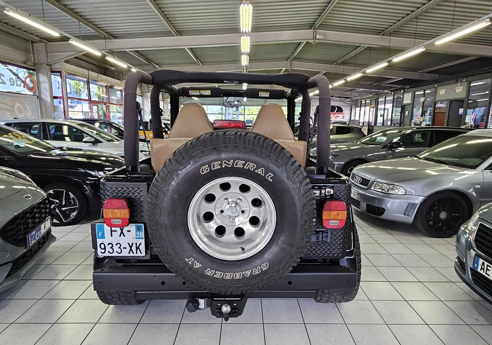 Vue arrière d'une Jeep Wrangler noire de 2000 avec roue de secours General Grabber et intérieur beige visible.