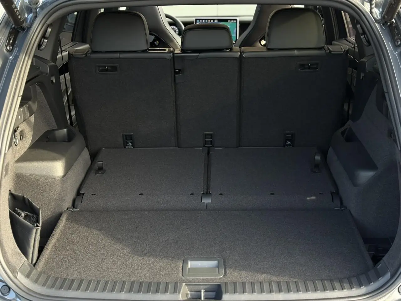 Vue du coffre arrière ouvert du Volkswagen Tayron 2.0 TDI gris dauphin avec banquette arrière relevée et espace de chargement plat.