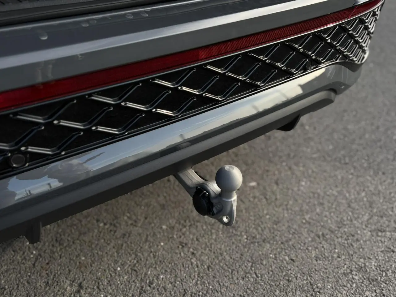 Gros plan sur l'attelage rabattable gris dauphin du Volkswagen Tayron 2025, avec calandre noire R-Line visible.