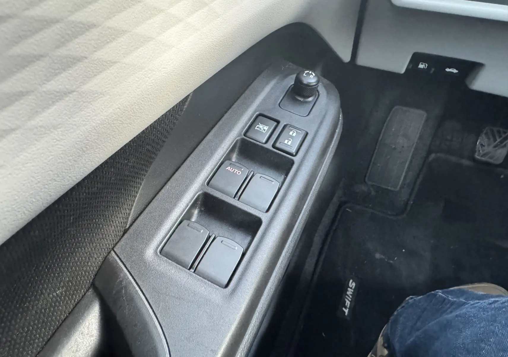 Gros plan sur les commandes de lève-vitres et rétroviseurs côté conducteur d'une Suzuki Swift blanche 2025.