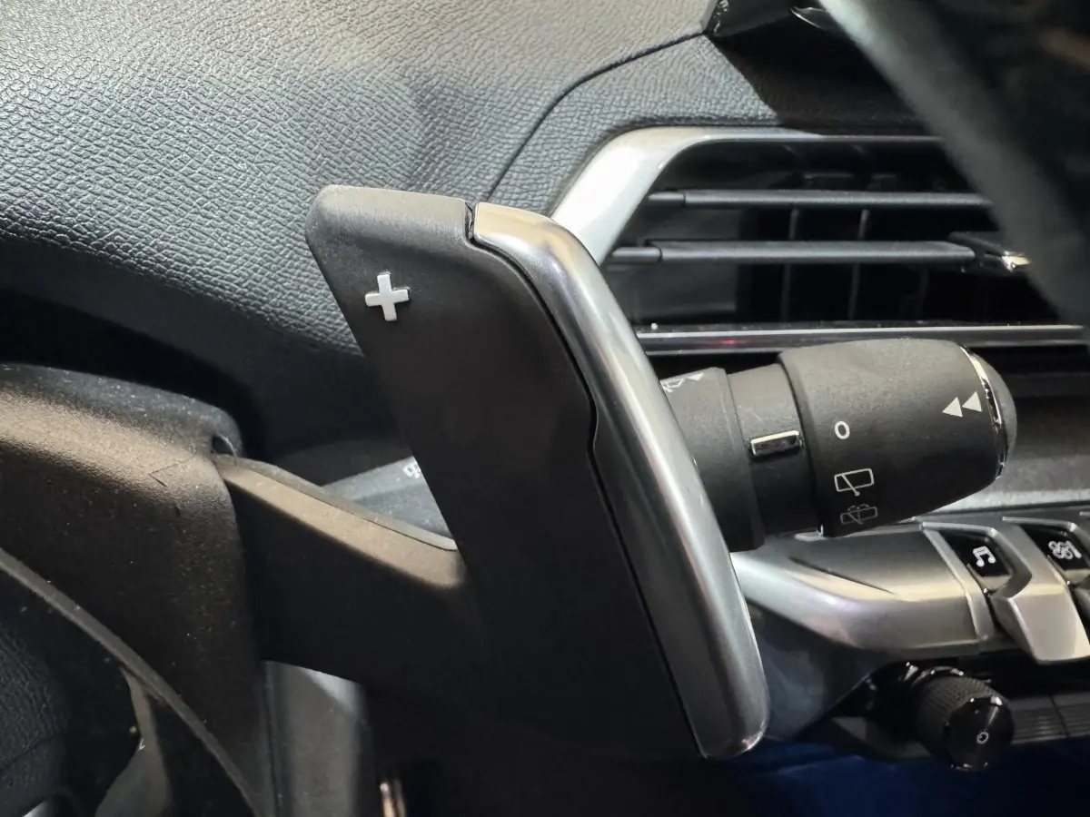 Gros plan sur la palette de changement de vitesse droite en plastique noir et métal dans l'habitacle du Peugeot 3008 gris clair.