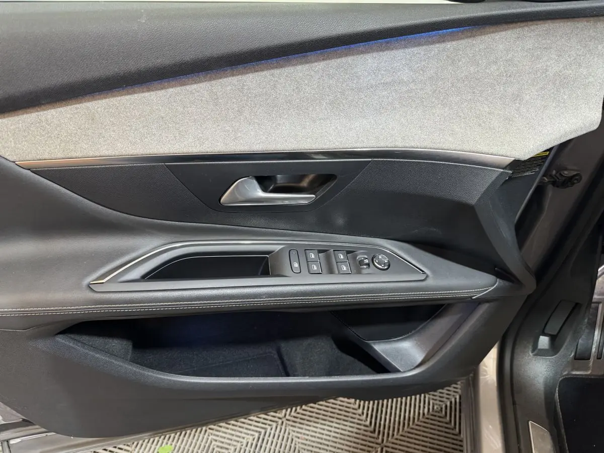 Intérieur côté gauche de la porte avant d'un Peugeot 3008 gris clair, avec commandes des vitres et poignée métallique.