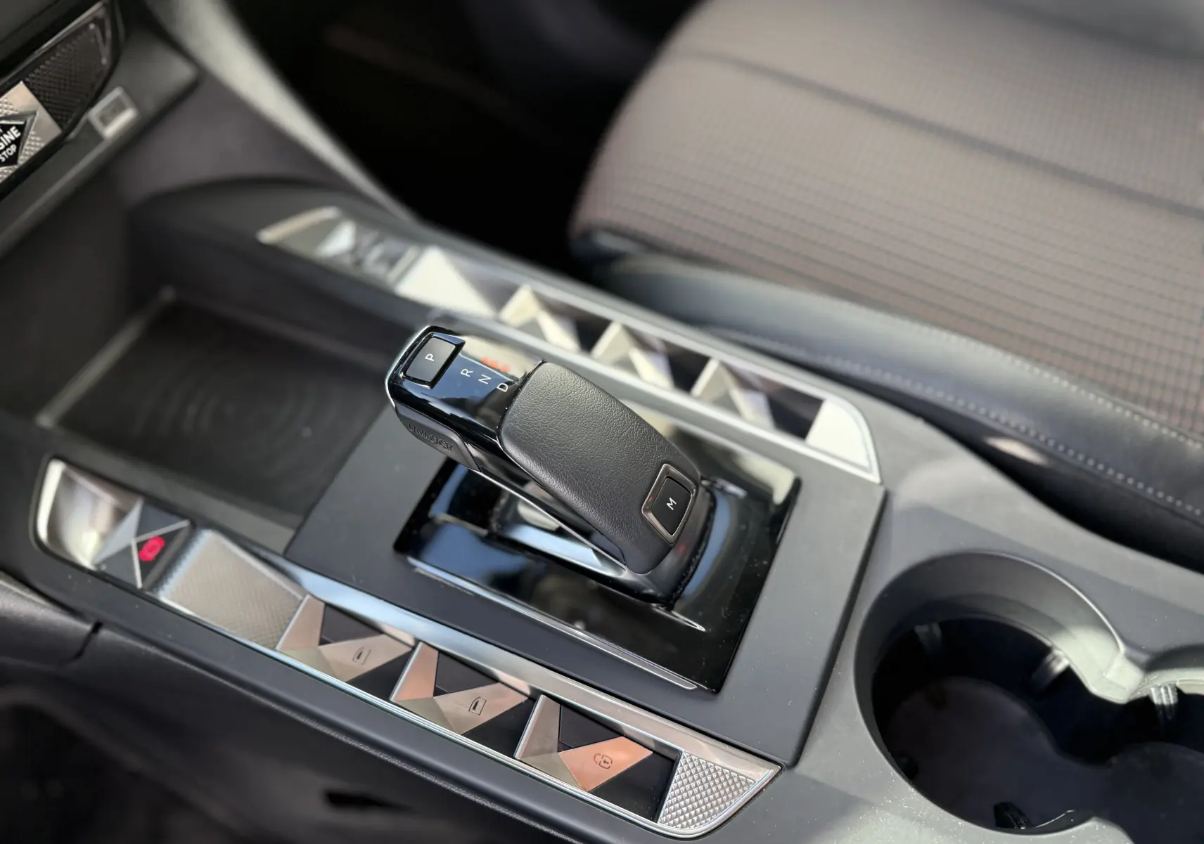 Gros plan sur la console centrale du DS3 hybride 2025, avec levier de vitesse automatique et sièges tissu gris à motifs.