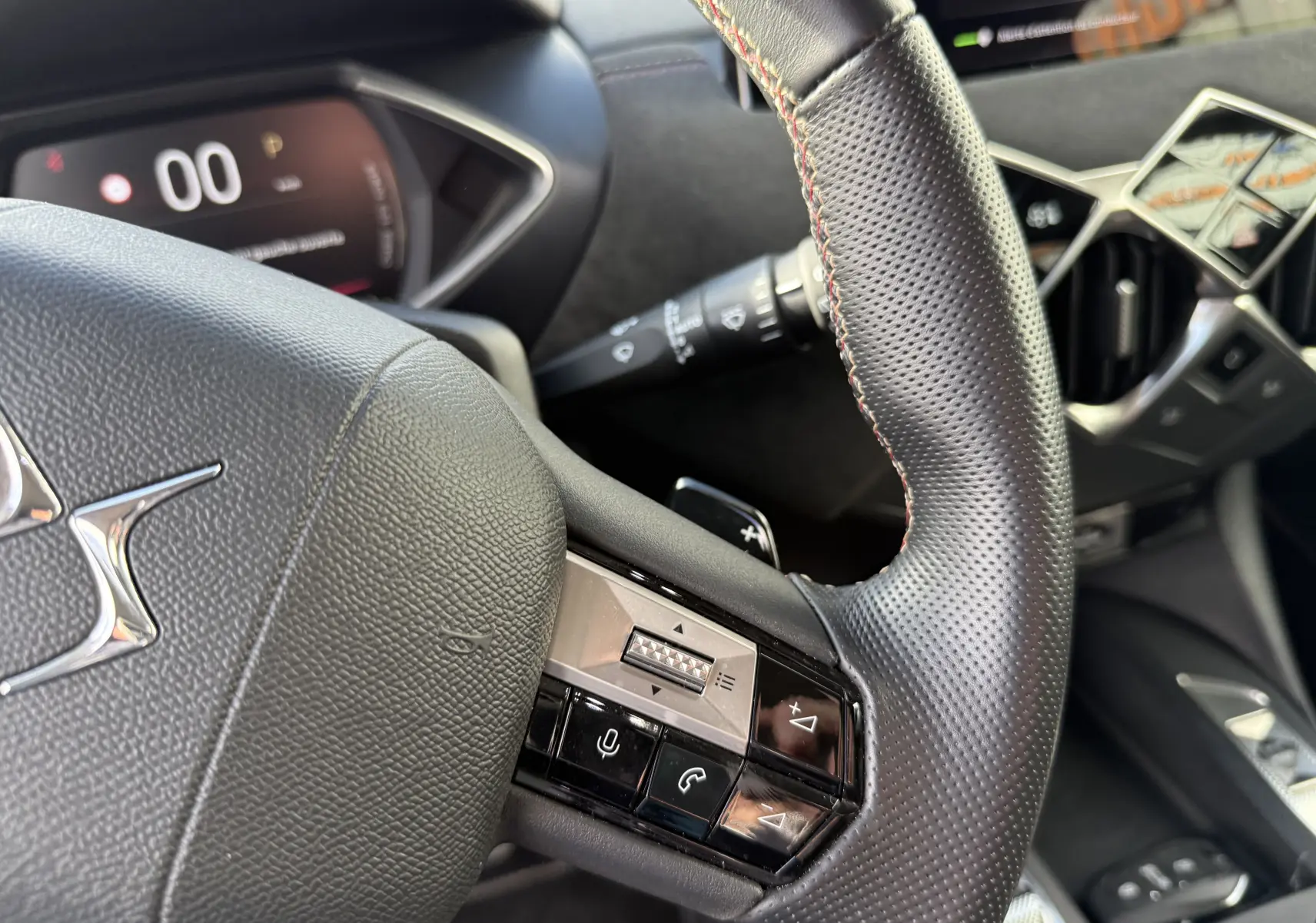 Gros plan sur le volant en cuir noir perforé du DS3 hybride 2025 avec commandes intégrées et tableau de bord numérique.