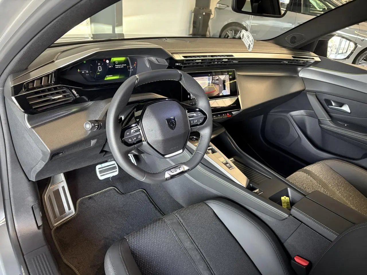 Intérieur avant droit de la Peugeot 308 GT 2025 avec volant cuir, combiné numérique et sellerie tri matières noire.