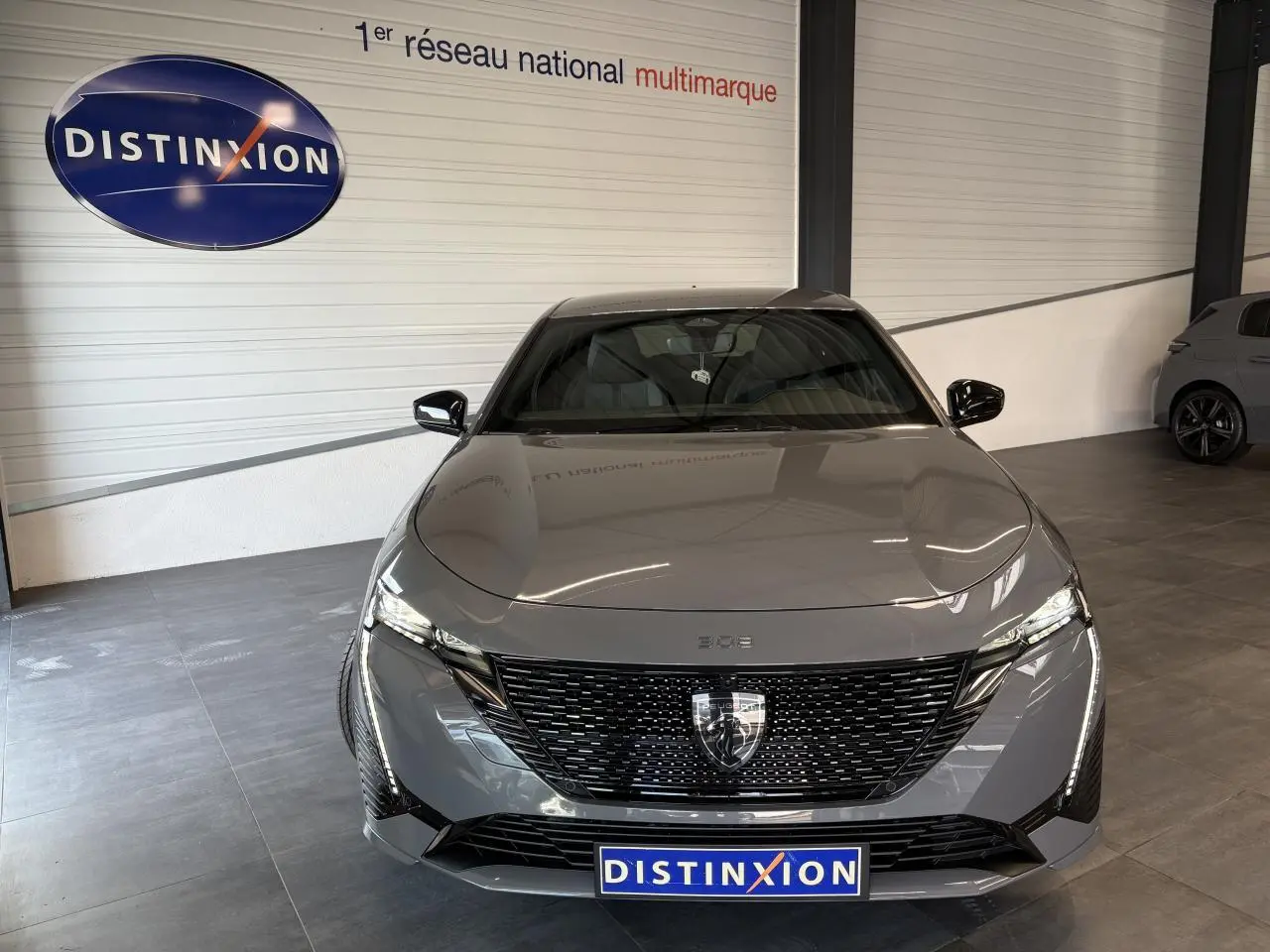 Vue avant frontale d'une Peugeot 308 GT 2025 gris selenium avec calandre noire brillante et logo lion distinctif.