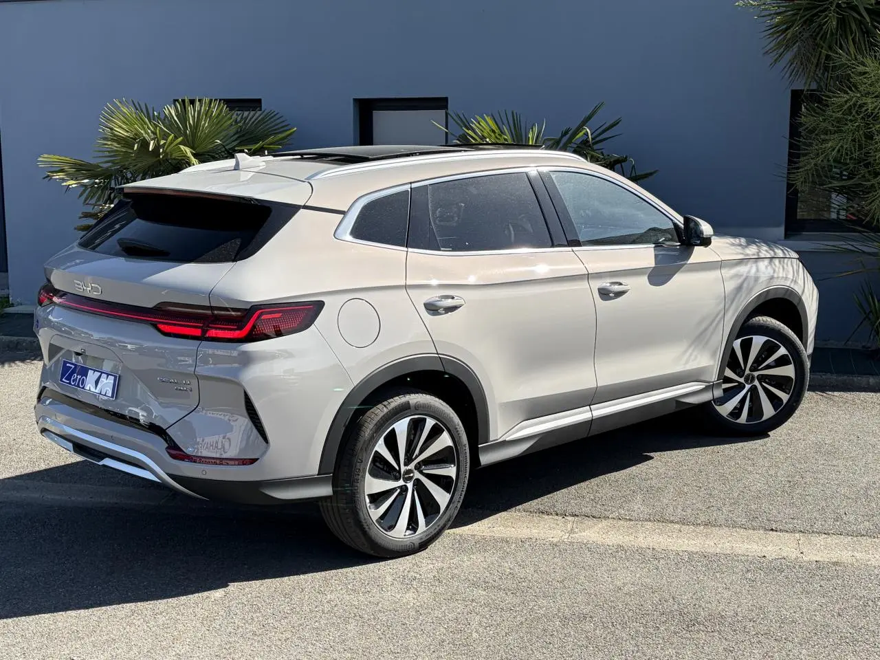 Vue 3/4 arrière droite du BYD SEAL U beige Boundless Cloud avec toit panoramique et feux arrière LED allumés.