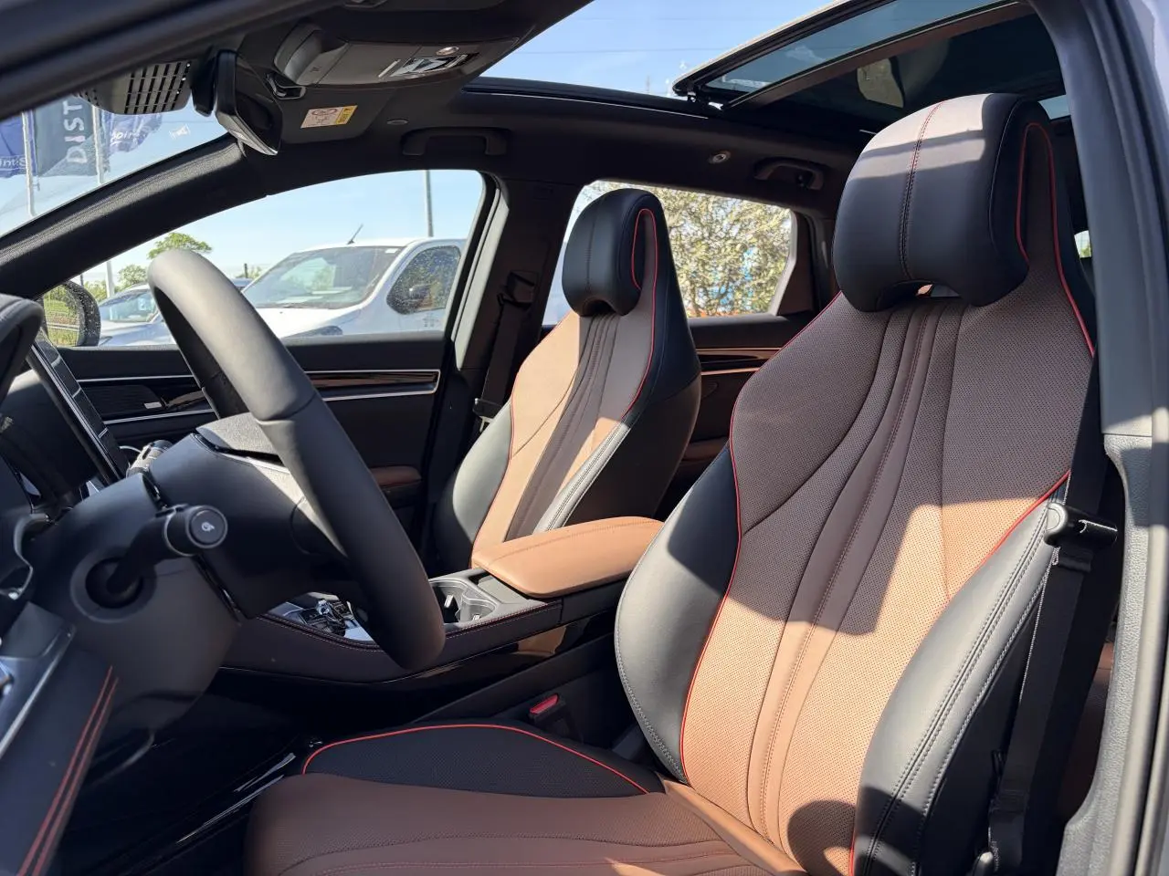 Intérieur du BYD SEAL U 2025 vu côté conducteur, sièges noir et brun avec surpiqûres rouges et toit panoramique.
