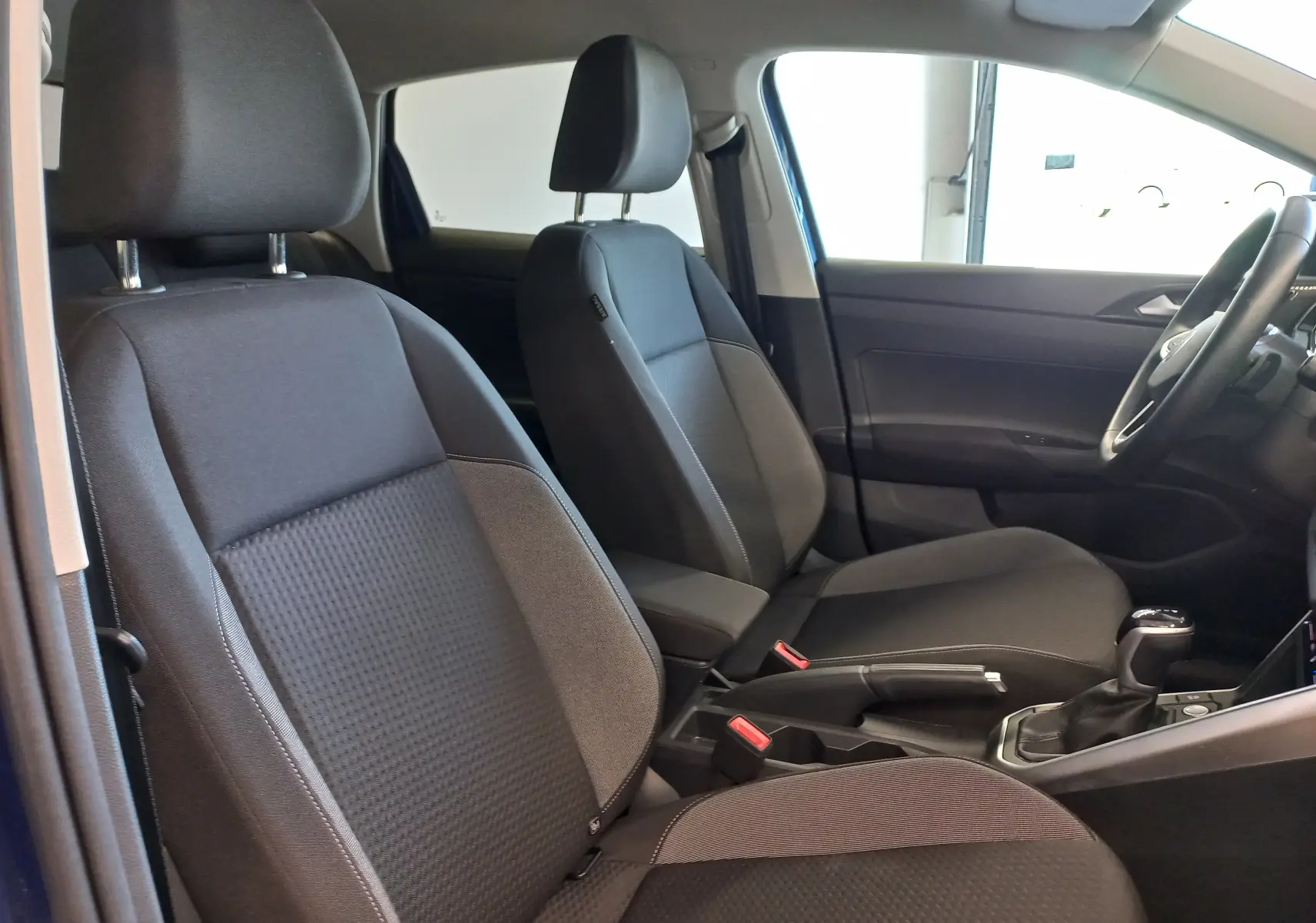 Vue intérieure côté droit du Volkswagen Taigo 2025 bleu récif, montrant les sièges avant en tissu noir et la console centrale.
