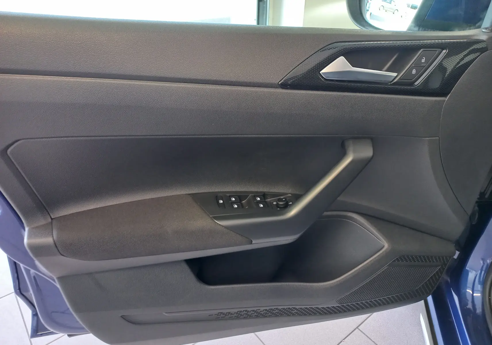 Vue intérieure côté gauche de la porte avant bleu récif du Volkswagen Taigo 2025 avec commandes de vitres et verrouillage.