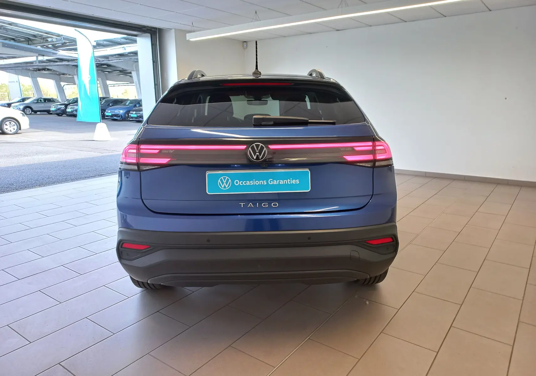 Vue arrière du Volkswagen Taigo bleu récif 2025 avec feux arrière LED allumés dans un showroom.